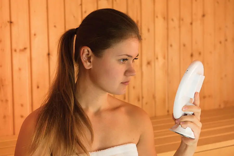 Young Woman Looking at a Small Mirror in a Sauna