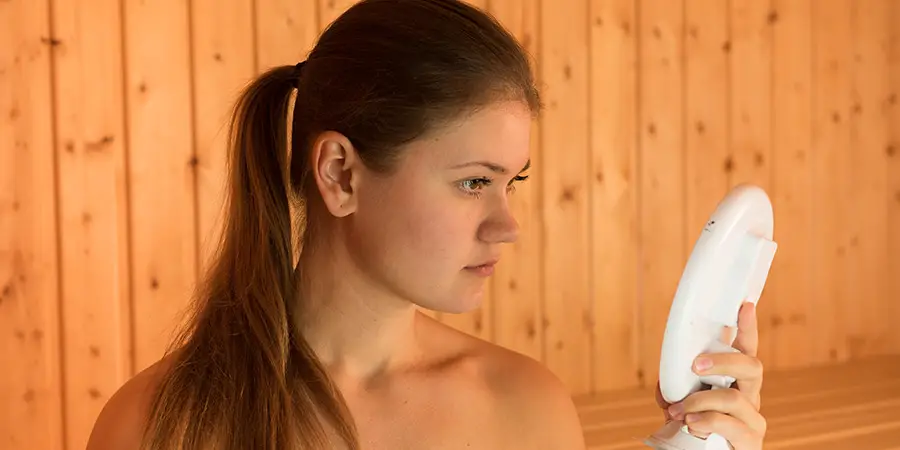 Young Woman Looking at a Small Mirror in a Sauna