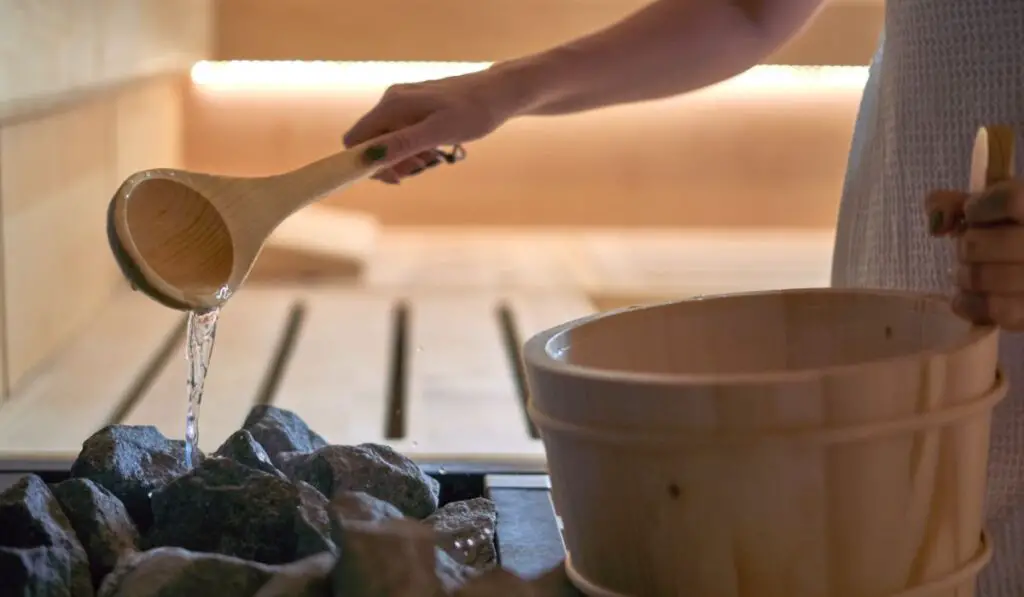 Woman pouring water into hot stone in sauna