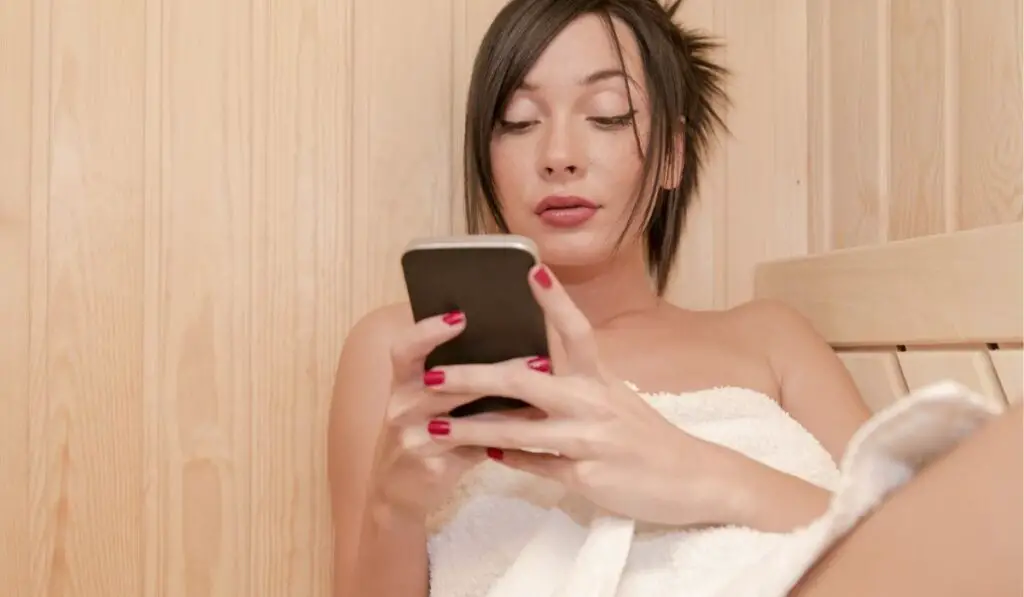 Young Woman Holding a Phone in a Sauna