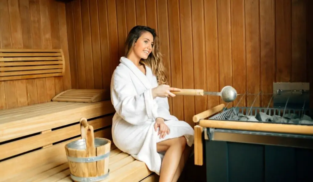 Beautiful woman in sauna pouring oils on hot stones